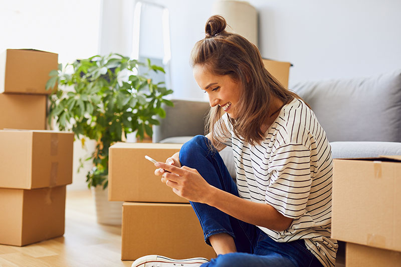 About-Us-Beautiful-young-woman-texting-while-moving-to-new-apartment